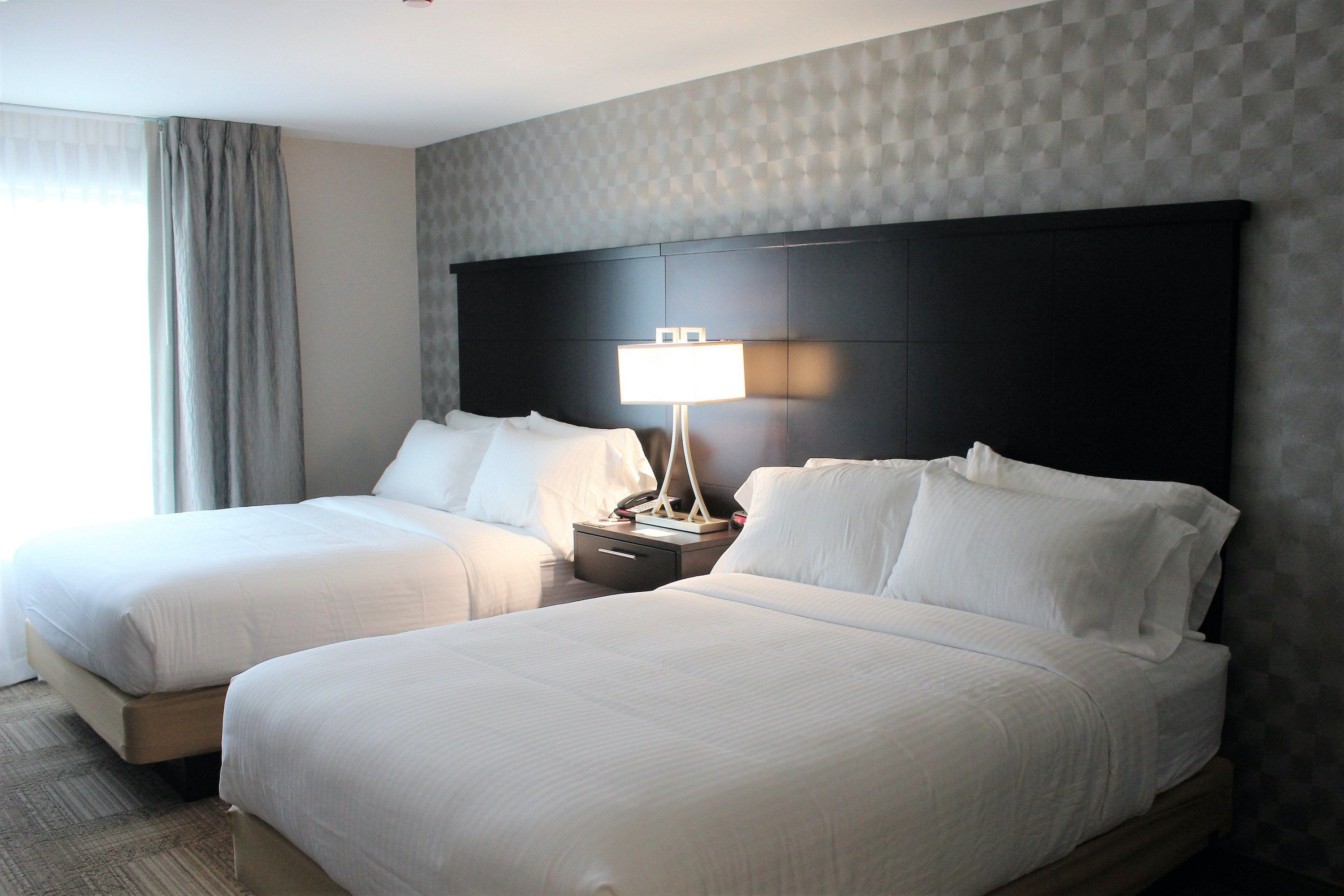 image Two queen beds with crisp white linens, a padded black headboard, and blackout curtains for a full night's sleep.