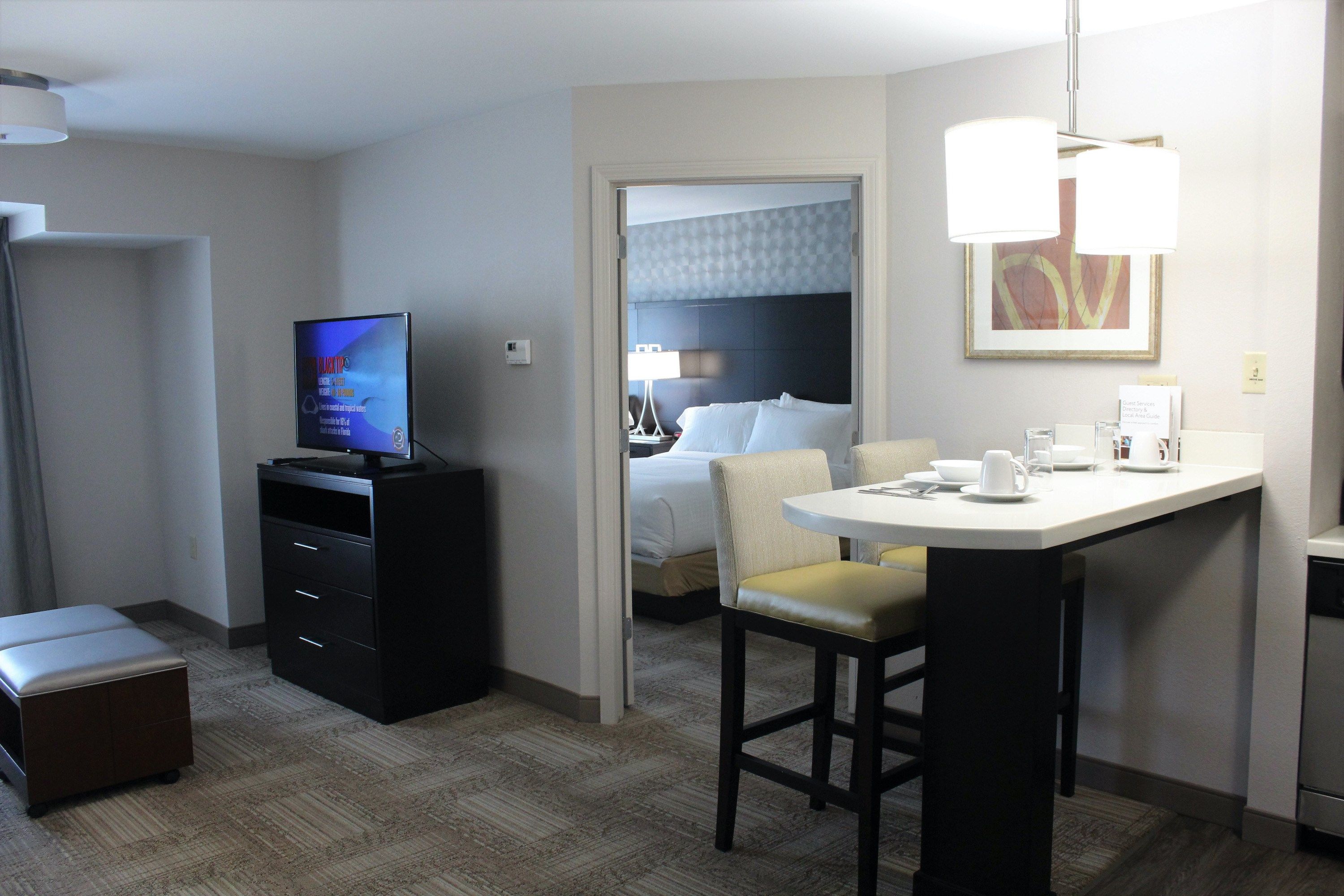 image Open-plan living area with flat-screen TV, bar counter seating, and a glimpse of the separate bedroom beyond.