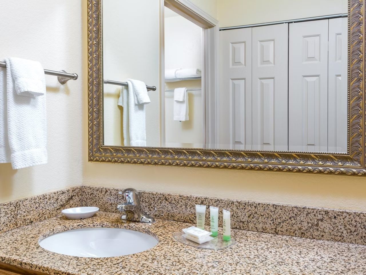 image Bathroom with granite countertop, round vessel sink, chrome faucet, and towels and toiletries neatly arranged below the mirror