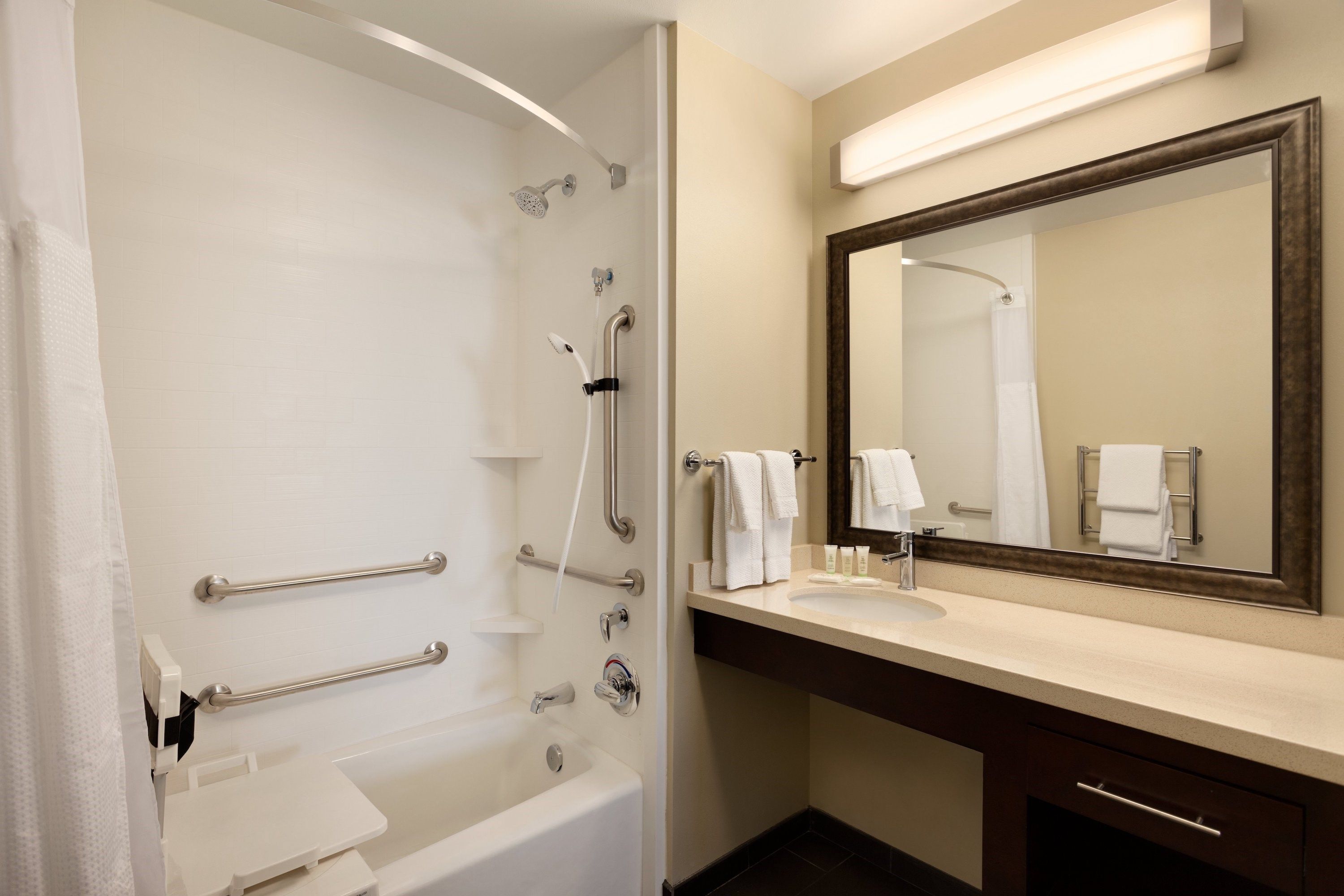 image Accessible bathroom with grab bars, adjustable showerhead, bathtub, double towel bars, mirror, and complimentary toiletries displayed
