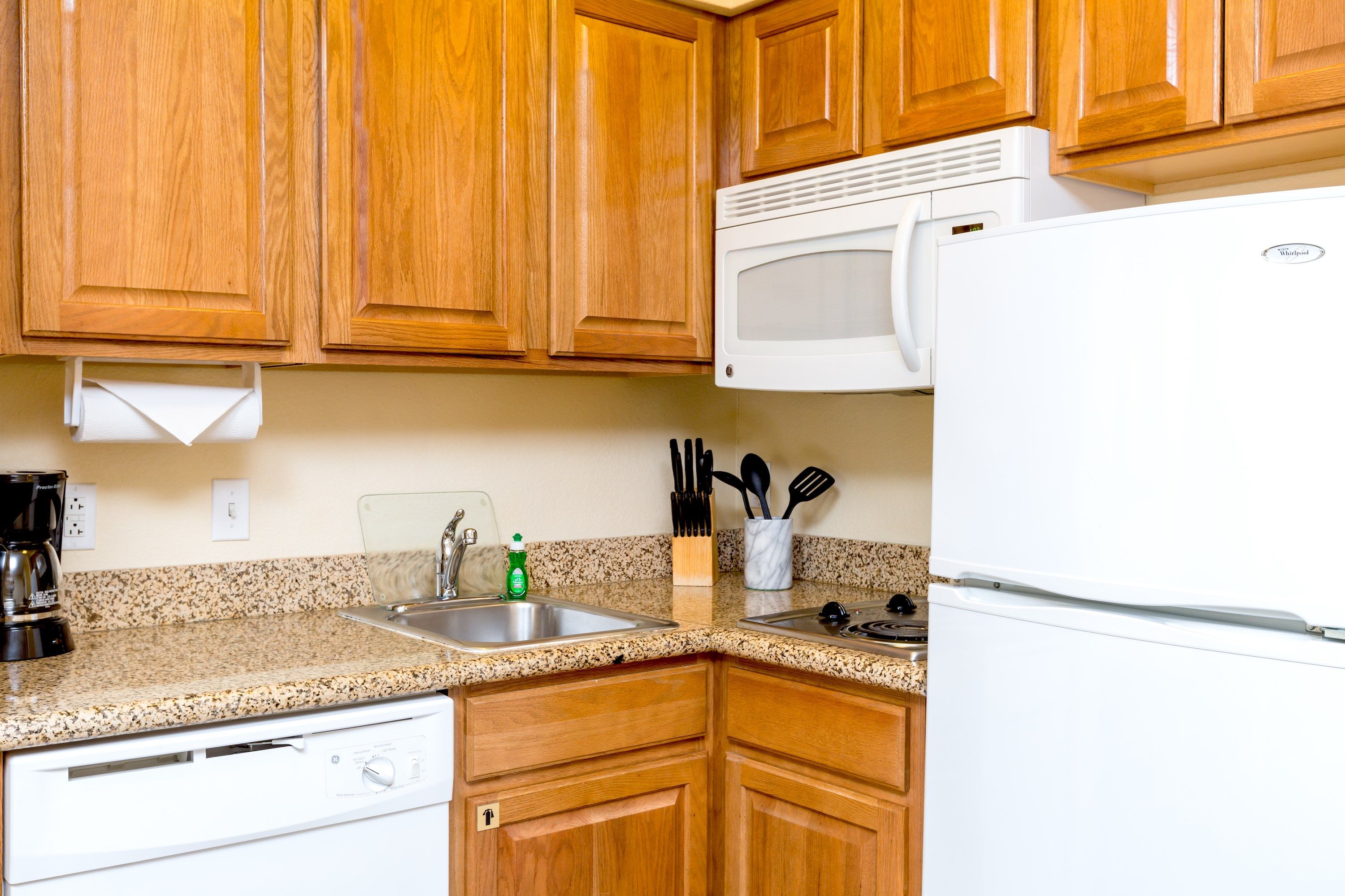 image Fully equipped kitchen with dishwasher, microwave, refrigerator, stove, sink, utensils, and coffee maker against wooden cabinetry