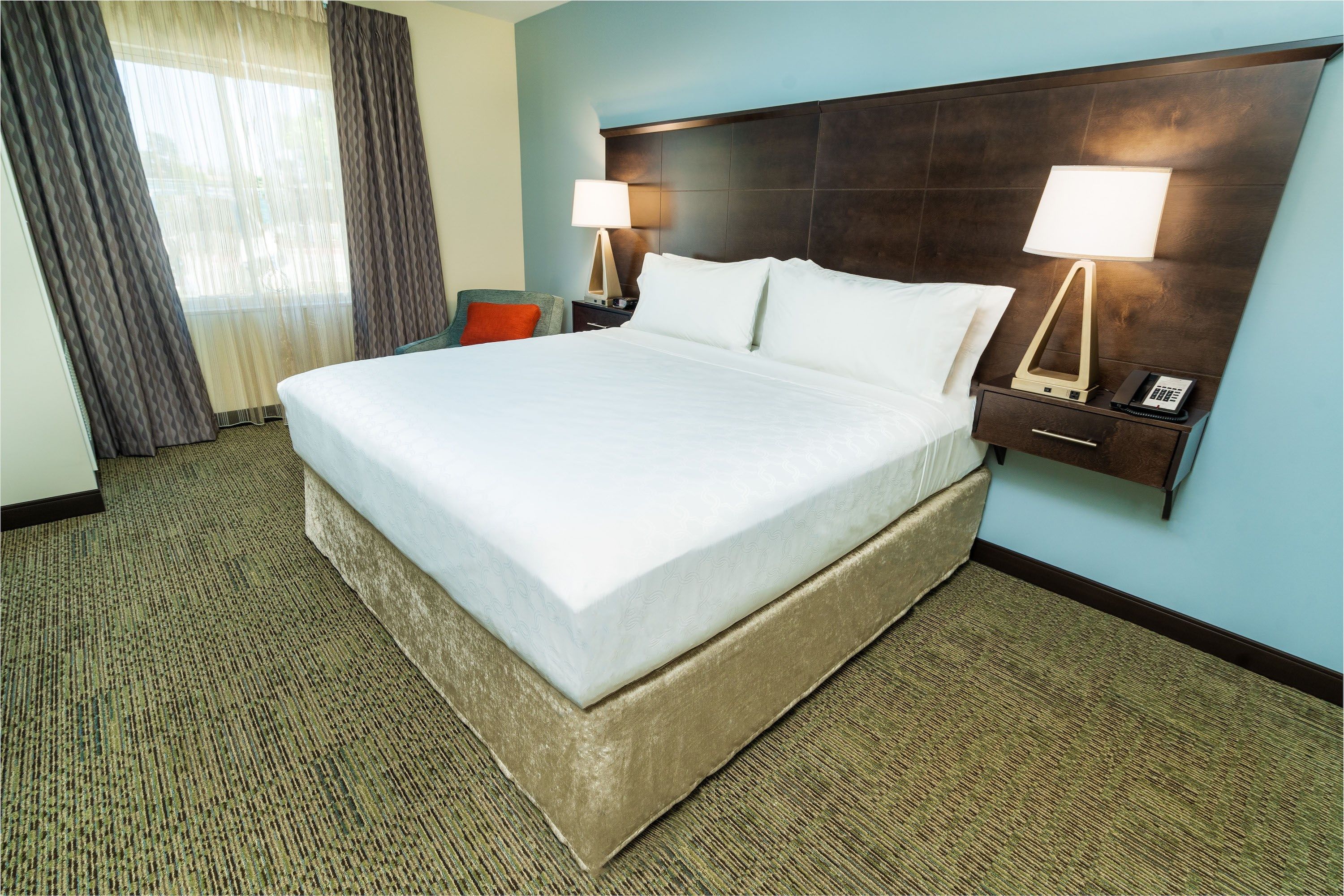 image Bedroom with a large bed, nightstand, lamp, and a corner chair.