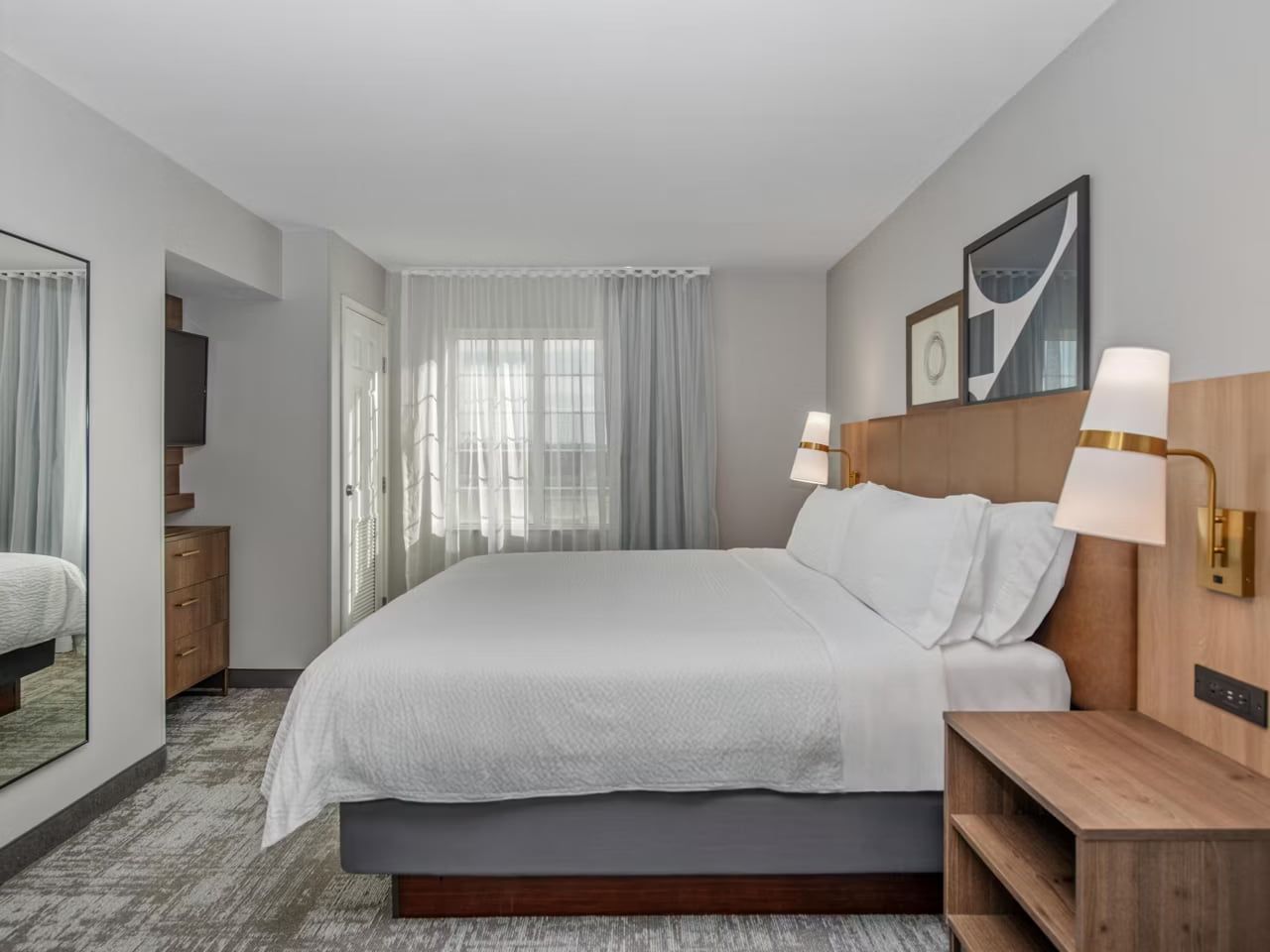 image A bedroom with a king-size bed, upholstered headboard with reading lights, and a full-length mirror.