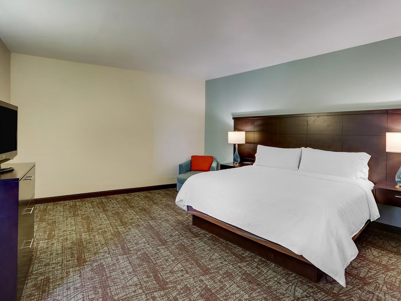 image Bedroom with king bed, dark wood headboard, wall-mounted flat-screen TV, dresser, and armchair.