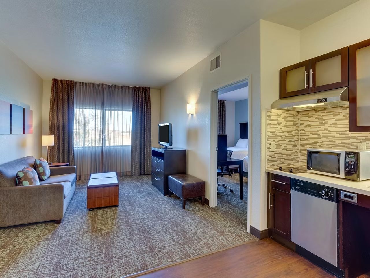 image Living space with sofa, coffee table, wall-mounted flat-screen TV, and kitchen with dishwasher, microwave, and dark wood cabinetry.