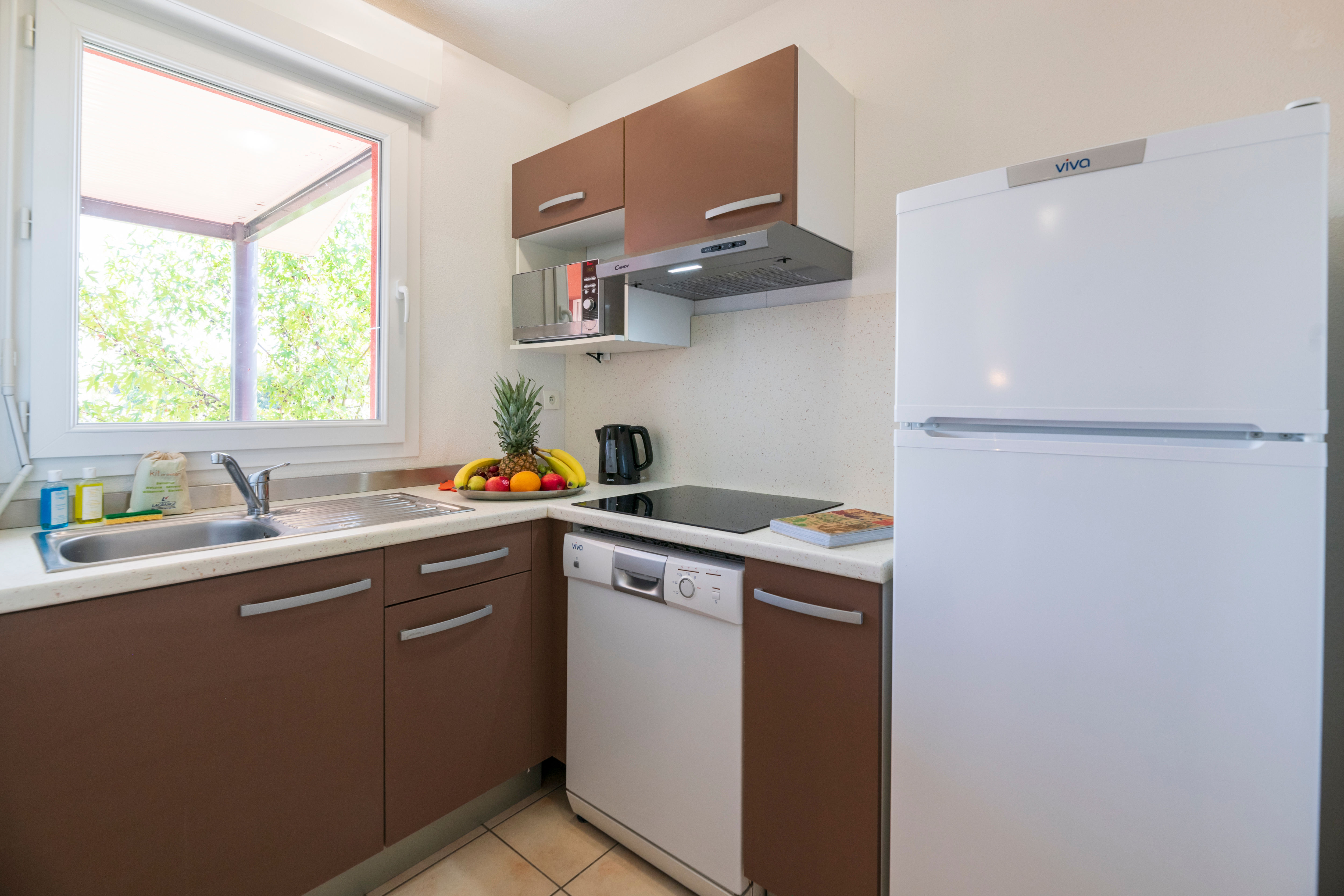 image Cook your favorite meals in this compact kitchenette with wood cabinetry and a bright window overlooking greenery