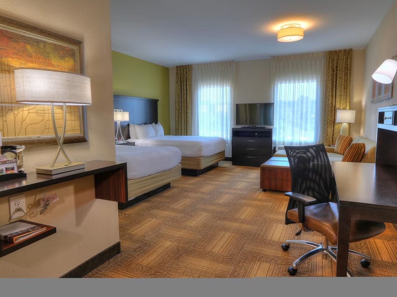 image Two double beds with black frames, ergonomic work desk, and flat-screen TV — natural light from the window