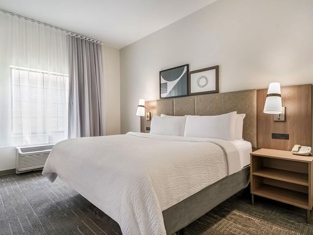 image King bed with upholstered headboard, wall-mounted lamps, and a bedside nightstand with telephone