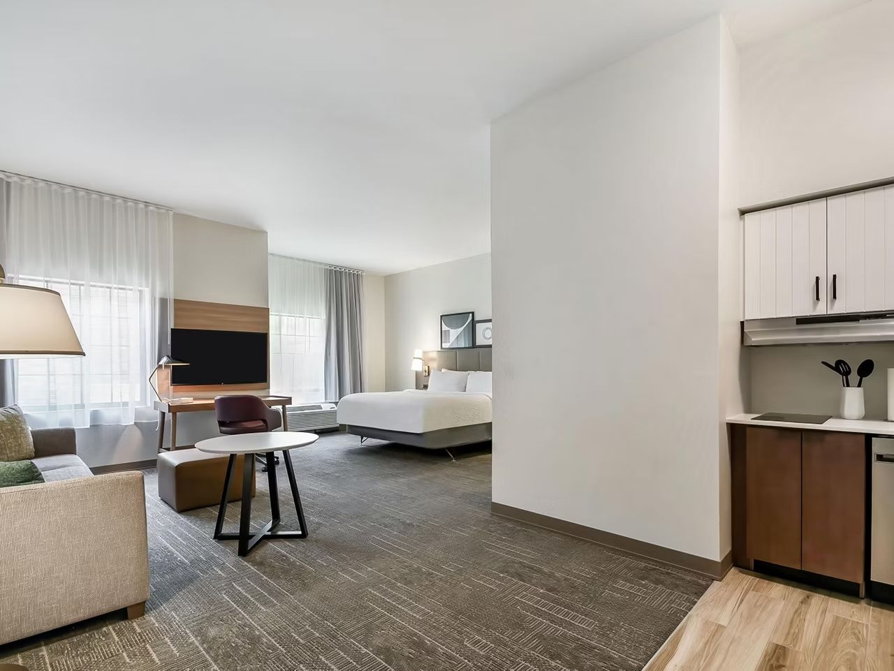 image King bed with white linens and sofa seating area, with kitchenette and flatscreen TV across the room