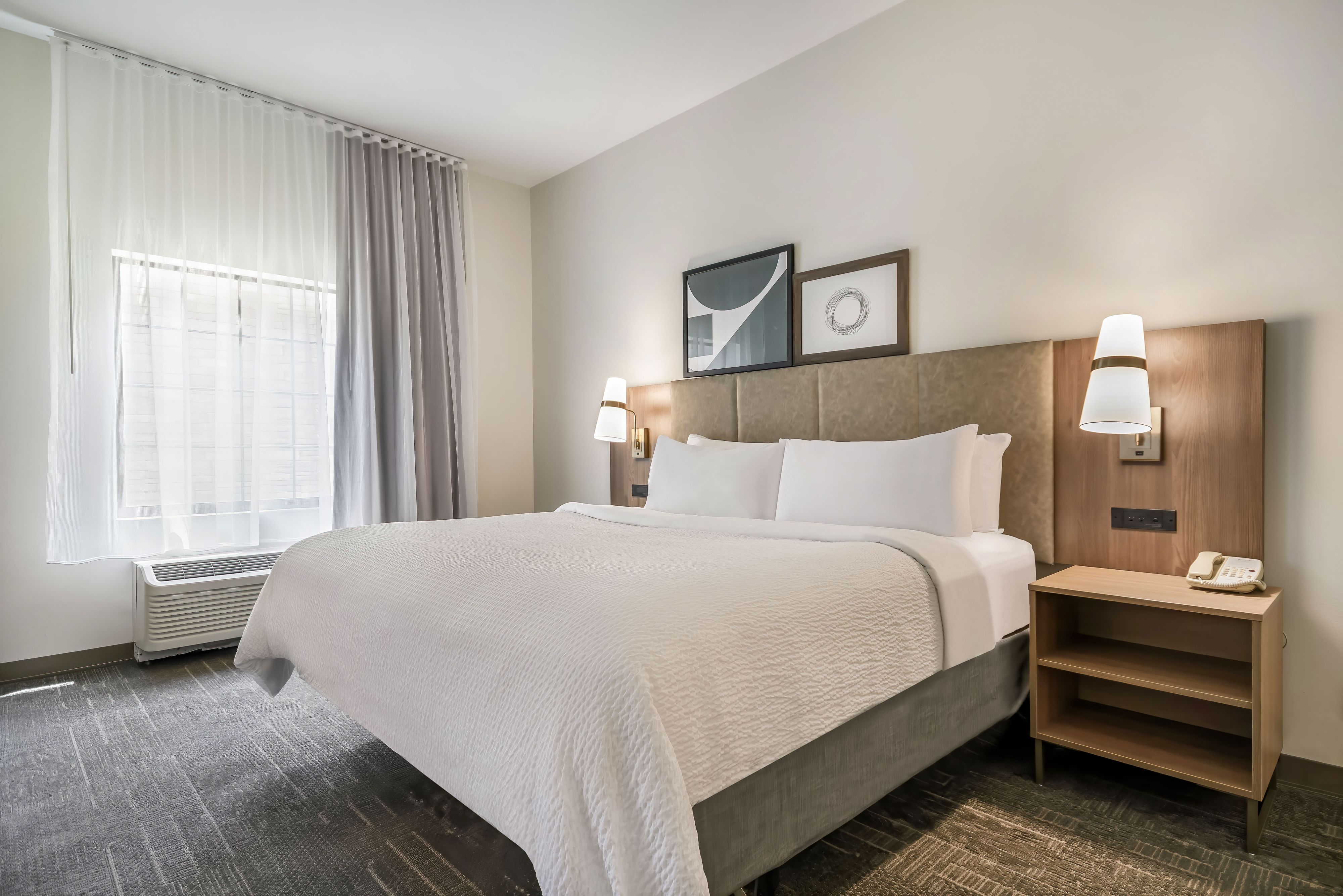 image King bed with white bedding, framed wall art, bedside lamps, and a sheer-curtained window