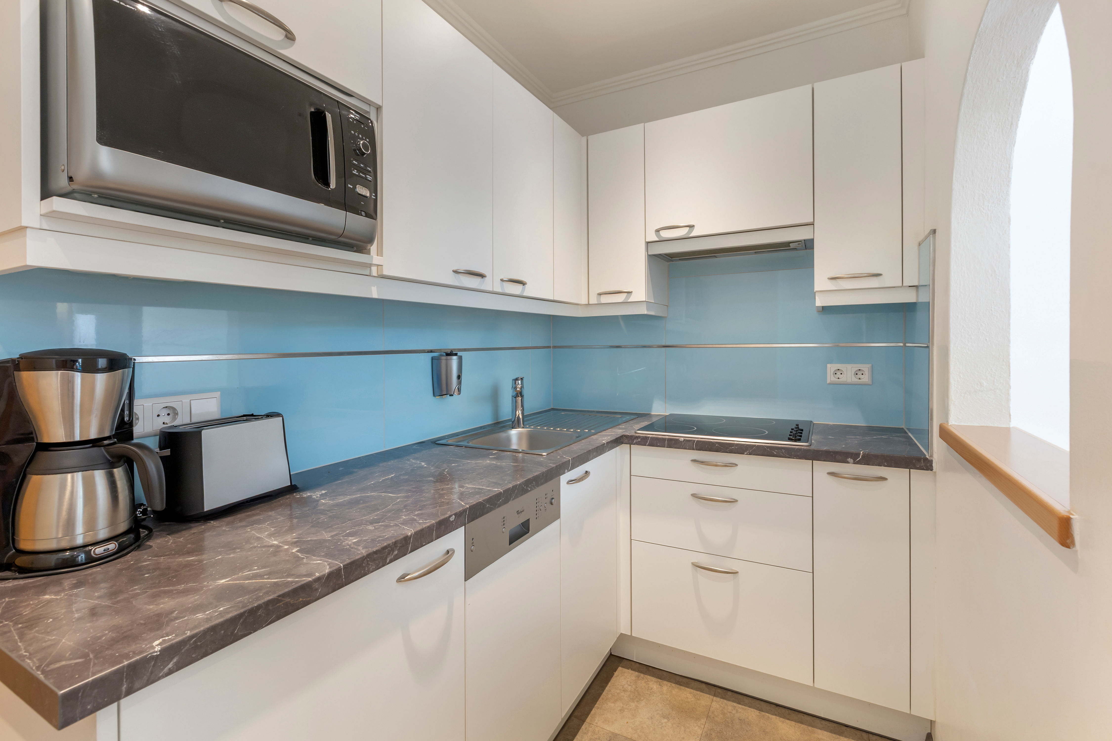 image The kitchen showcases sleek, white cabinetry and a contemporary style, equipped with essential appliances such as a stove and coffee machine, making cooking a delight.