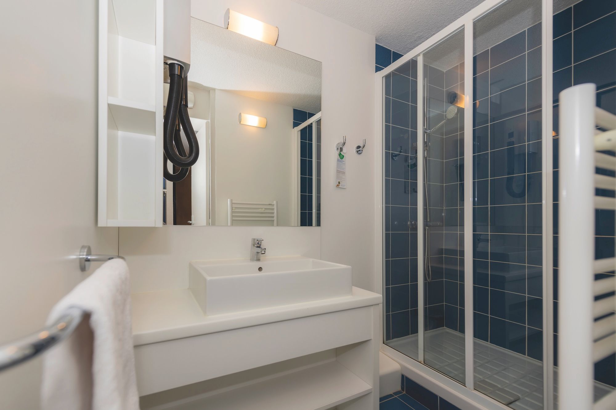 image Blue and white tiles surround the washbasin, the glass-enclosed shower and the towel rack in the bathroom