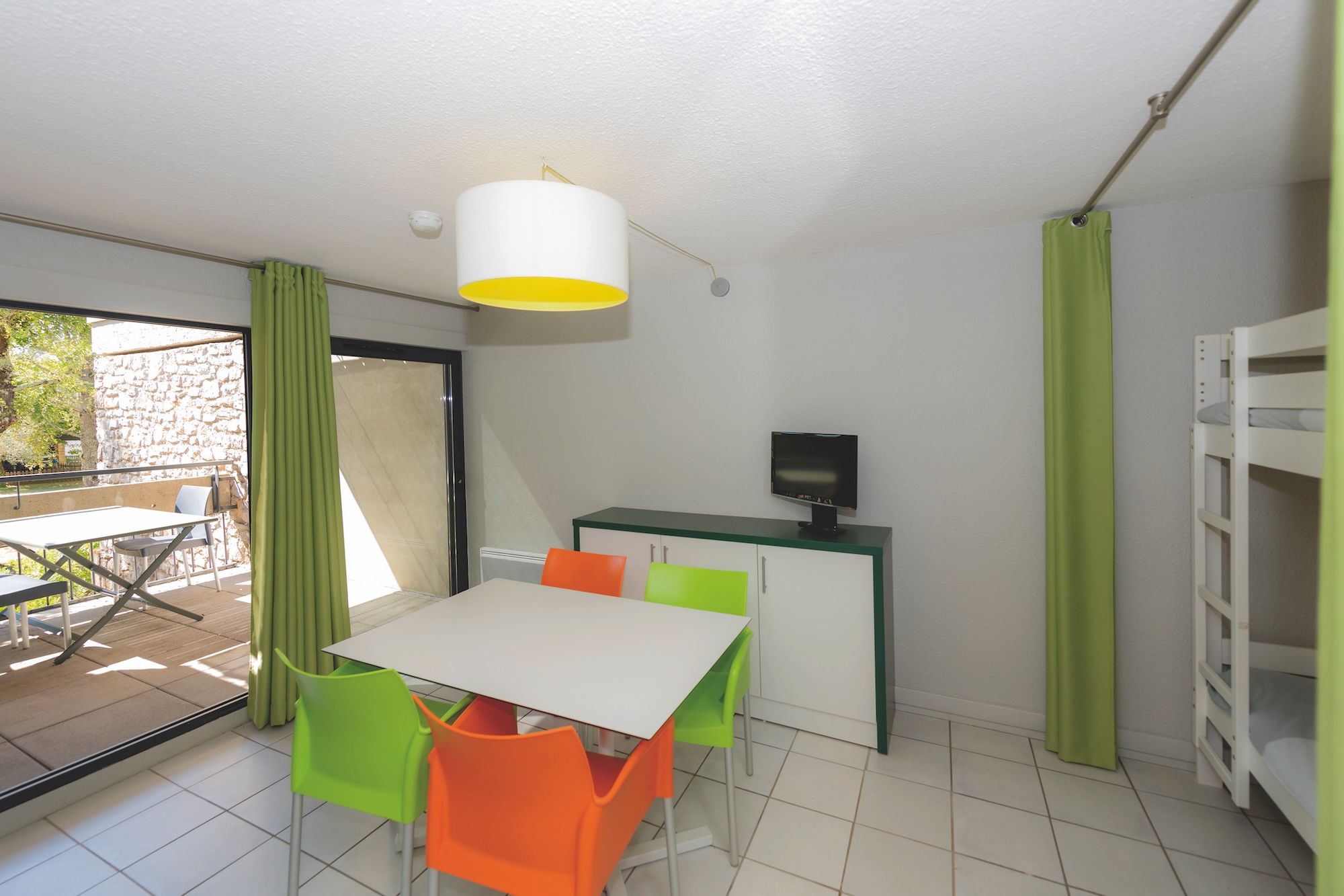 image Orange, green and white chairs surround the dining table, with the bunk bed stairs behind and the terrace beyond the sliding doors