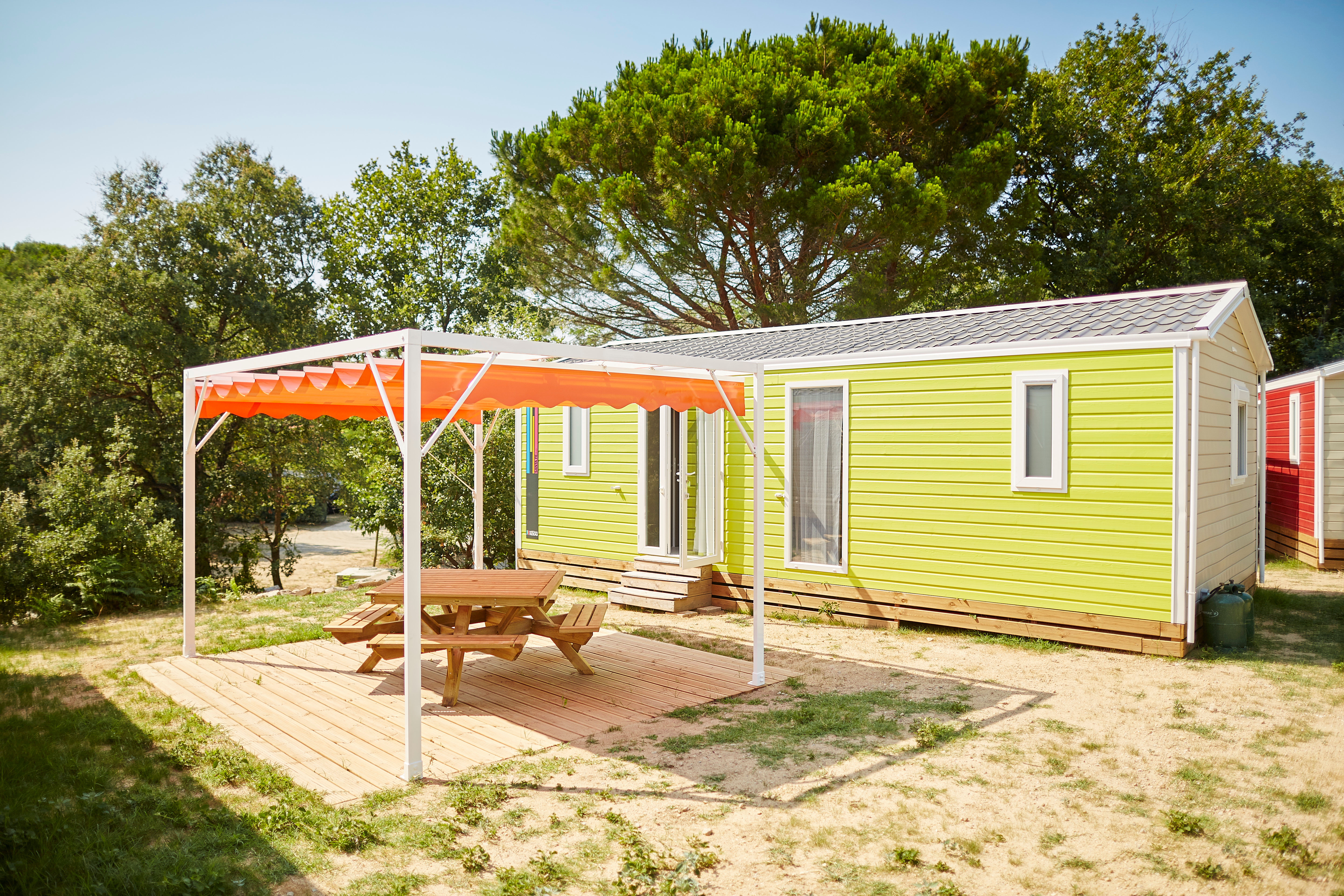 image Charming mobil-home featuring a shaded deck with an orange awning and picnic table nestled among trees.