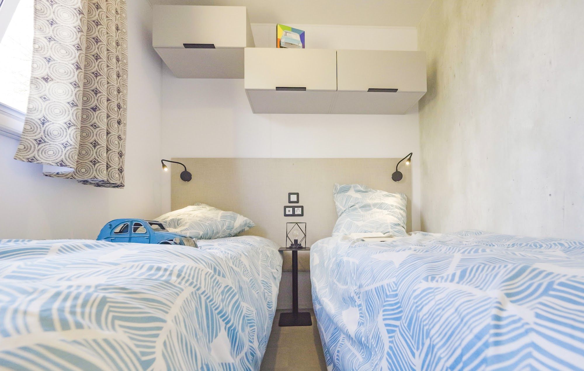 image Twin beds with blue patterned sheets and a toy on the nightstand.