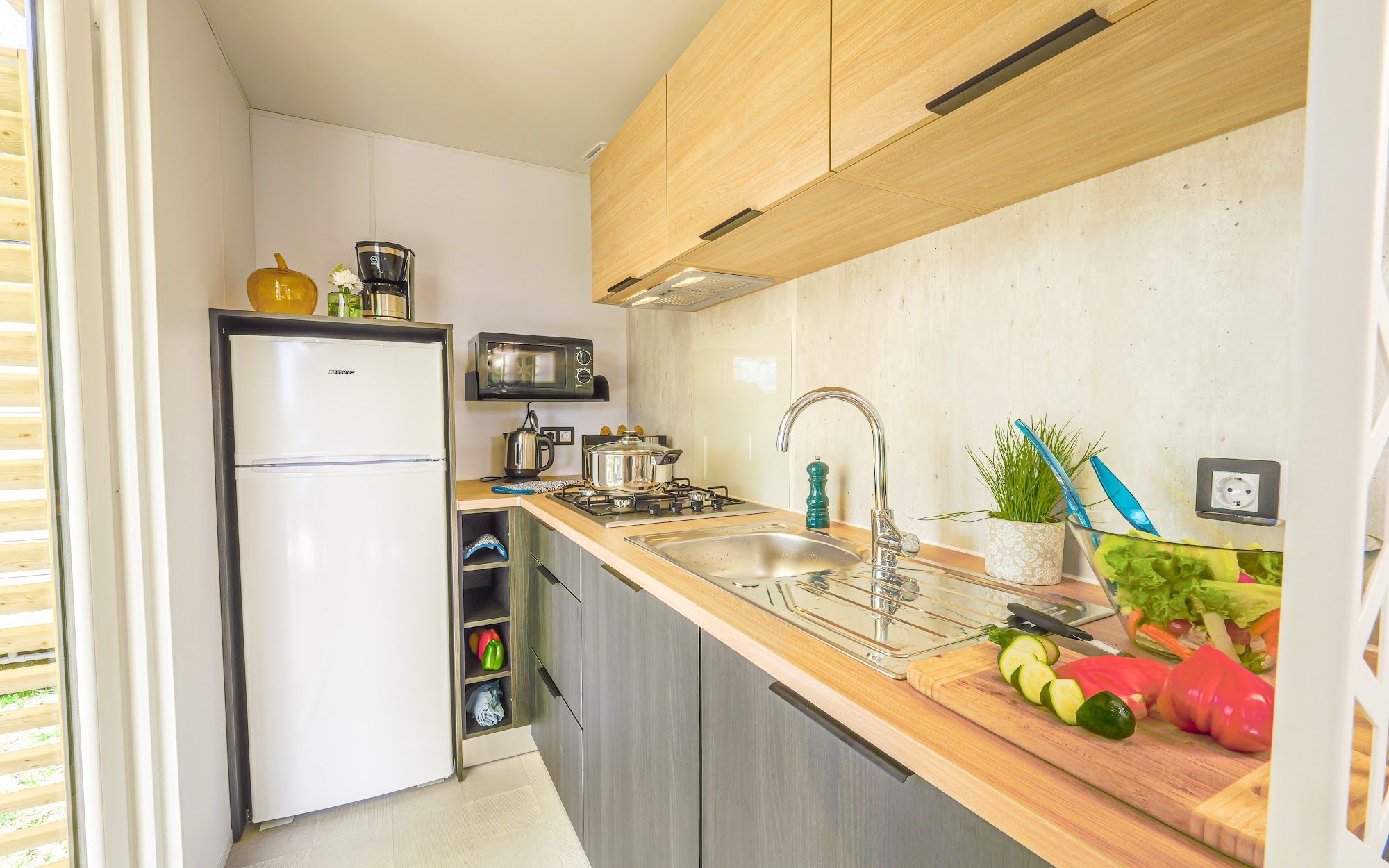 image Kitchen space with cooking supplies, vegetables, and a refrigerator.