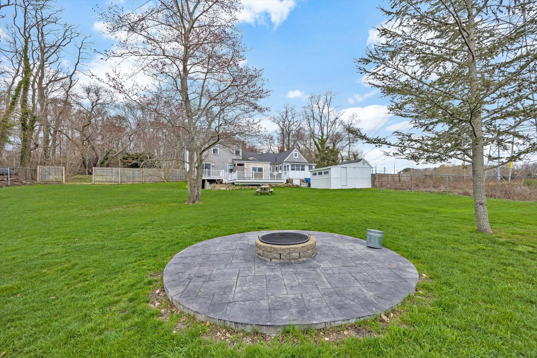 image Stone fire pit on a paved area in the backyard — two-story grey house with deck and shed behind