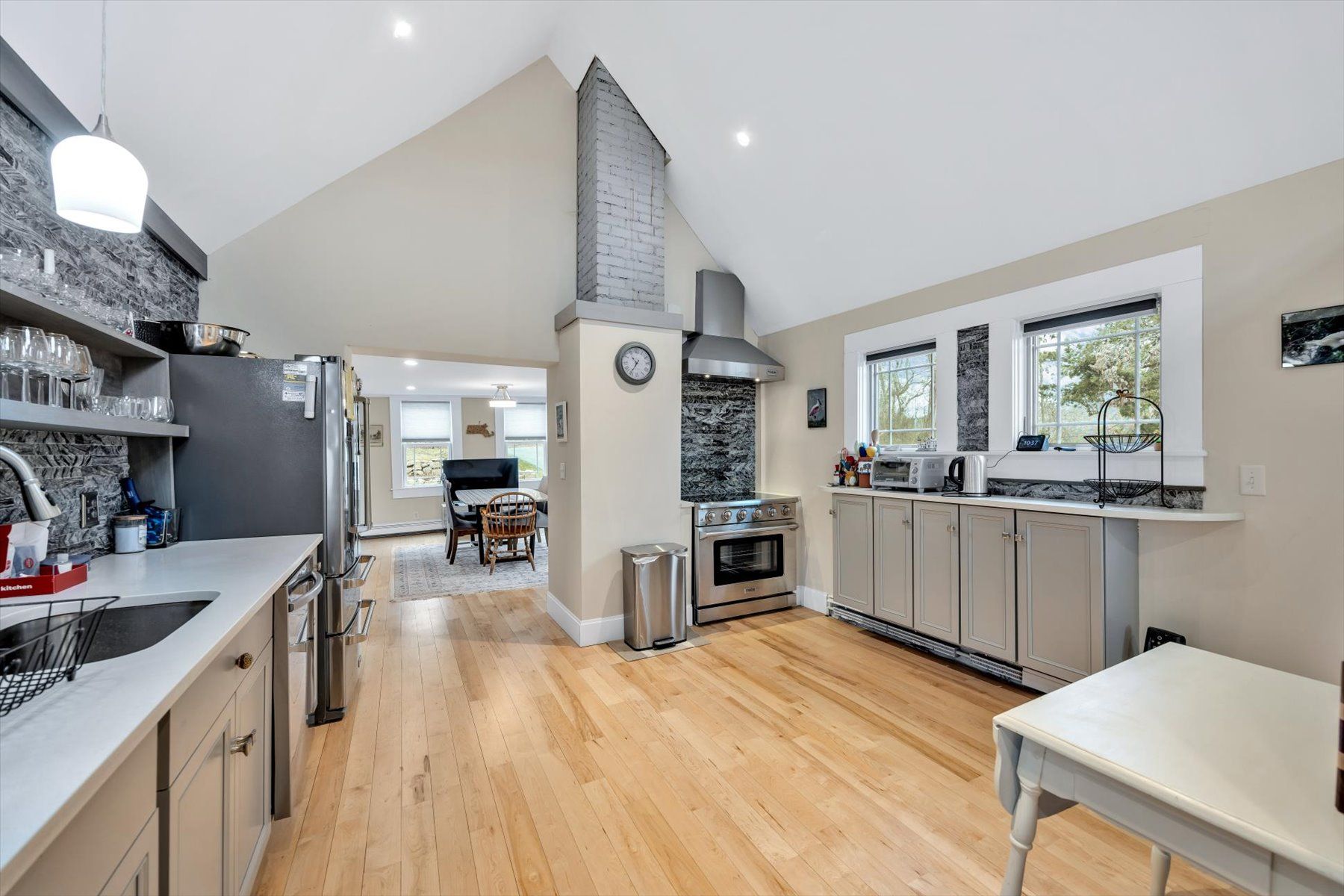 image Kitchen with gray cabinets, stainless steel stove and fridge, two windows, and a small wooden table
