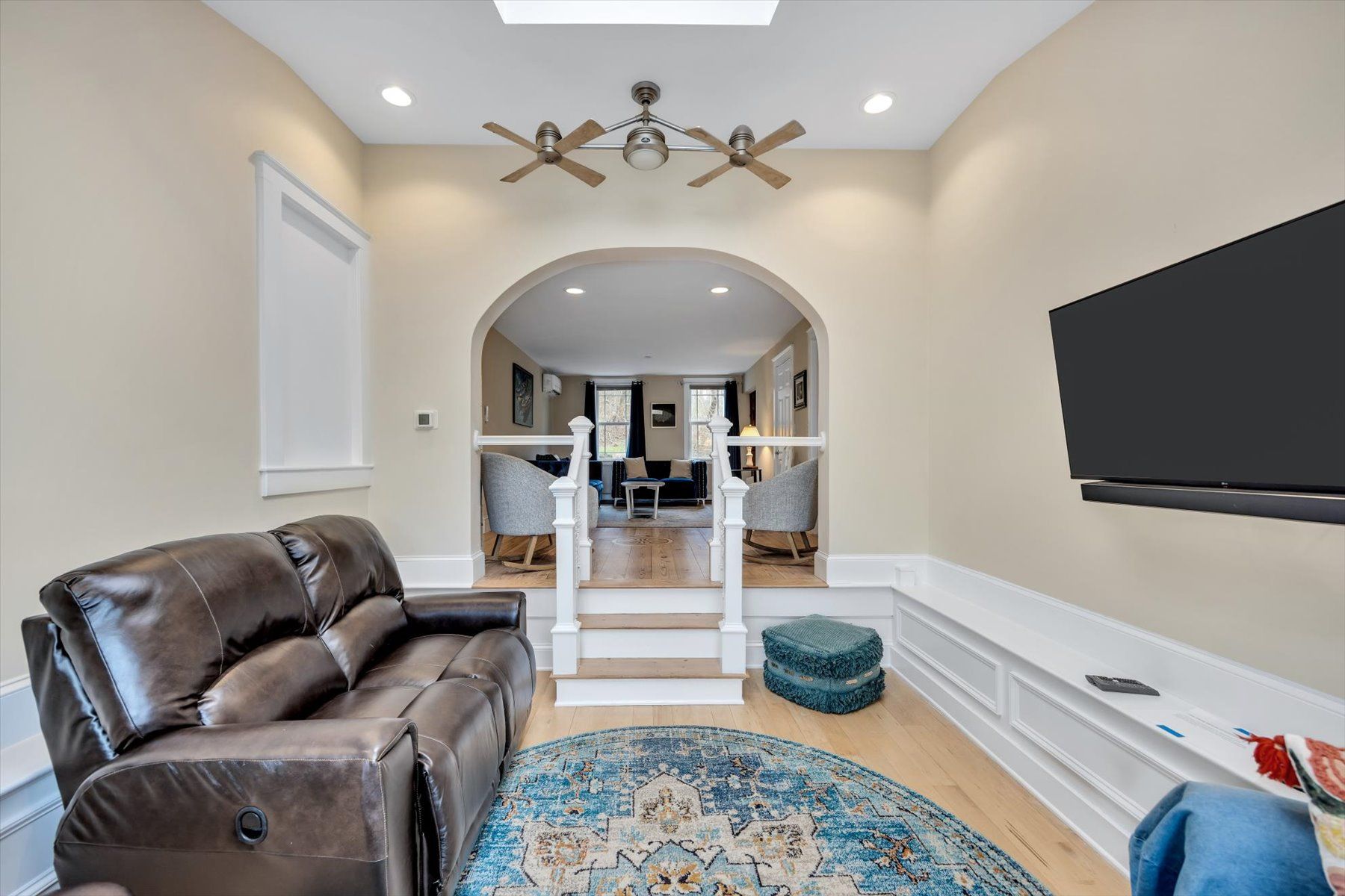 image Brown leather sofa, grey chairs, flat-screen TV, and ceiling fan — living room through the archway