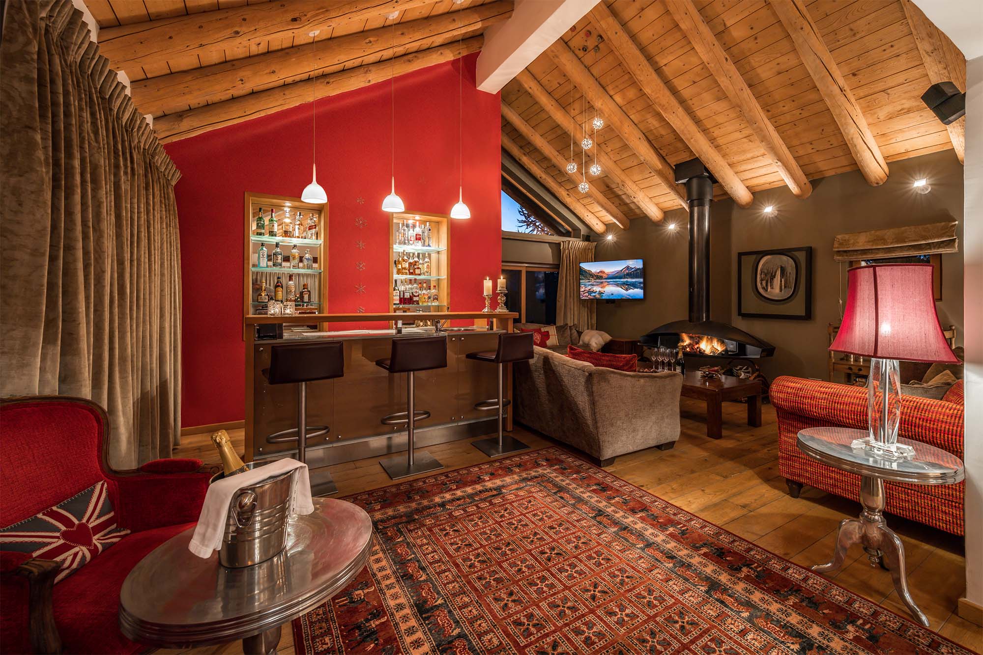 image Enjoy the ambiance of this elegant living area, boasting rich red decor, a large flat-screen TV, and a vintage-inspired rug. The high wooden ceilings and ambient lighting make it an ideal spot for family gatherings and movie nights.