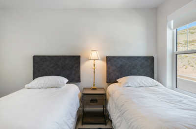 A serene bedroom setting featuring twin beds with textured dark gray headboards and a golden-toned lamp illuminating the minimalist space.