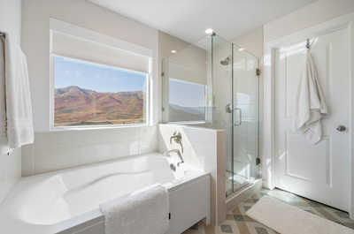 A bright and airy master bathroom adorned with modern fixtures, geometric floor tiles, and a spacious mirrored vanity reflecting a picturesque mountain view