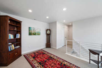 Enjoy this bright and spacious loft featuring a classic wooden bookshelf, vibrant forest artwork, a traditional grandfather clock, and a richly patterned oriental rug, all under modern recessed lighting