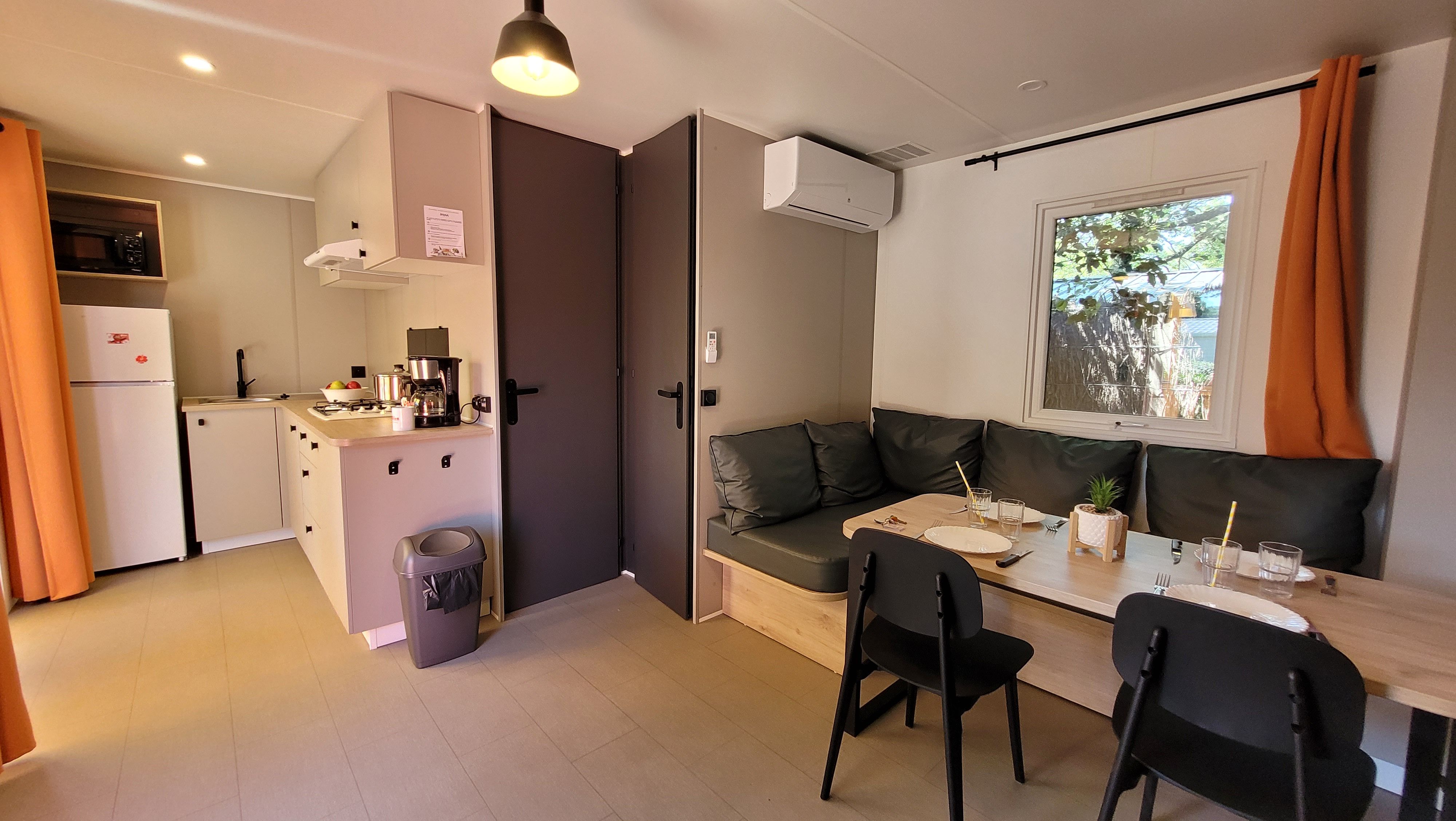 image A stylish and spacious 28 m² mobile home interior at Camping L’Orée du Bois, featuring an inviting kitchen and a cozy dining area with ample seating.