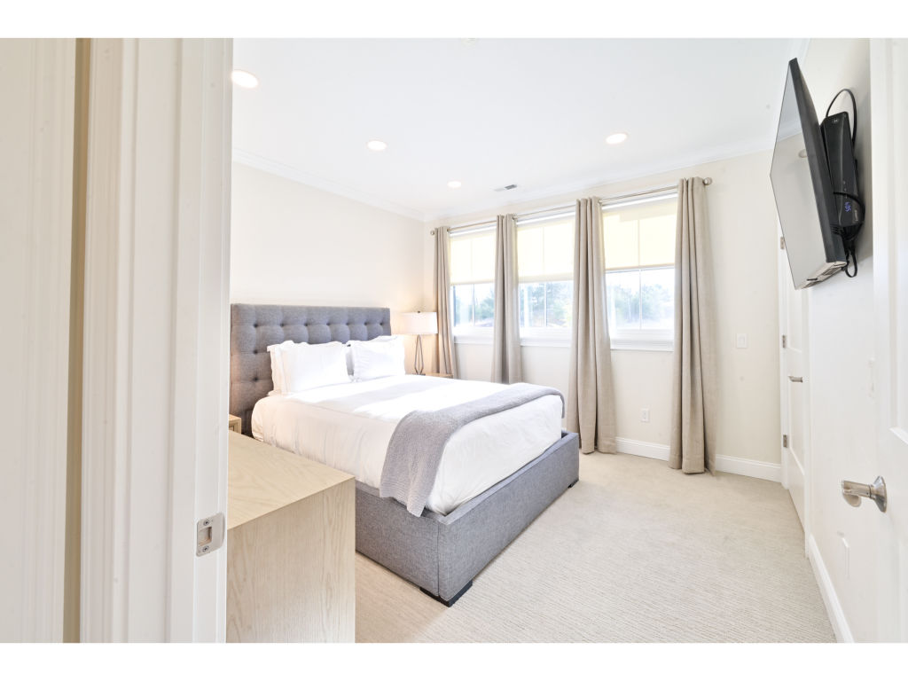 image Bright and spacious bedroom featuring a comfortable plush bed, flat-screen TV, and large windows for plenty of natural light.