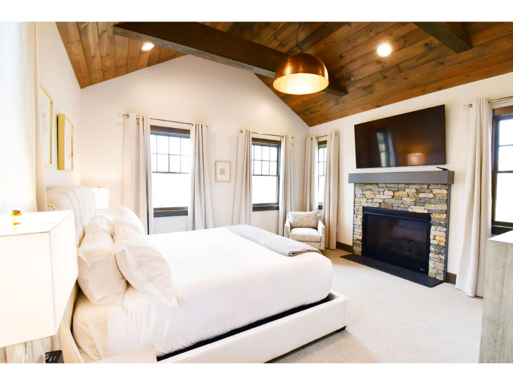 image Spacious bedroom with vaulted wooden ceilings, a cozy fireplace, and luxurious bedding.