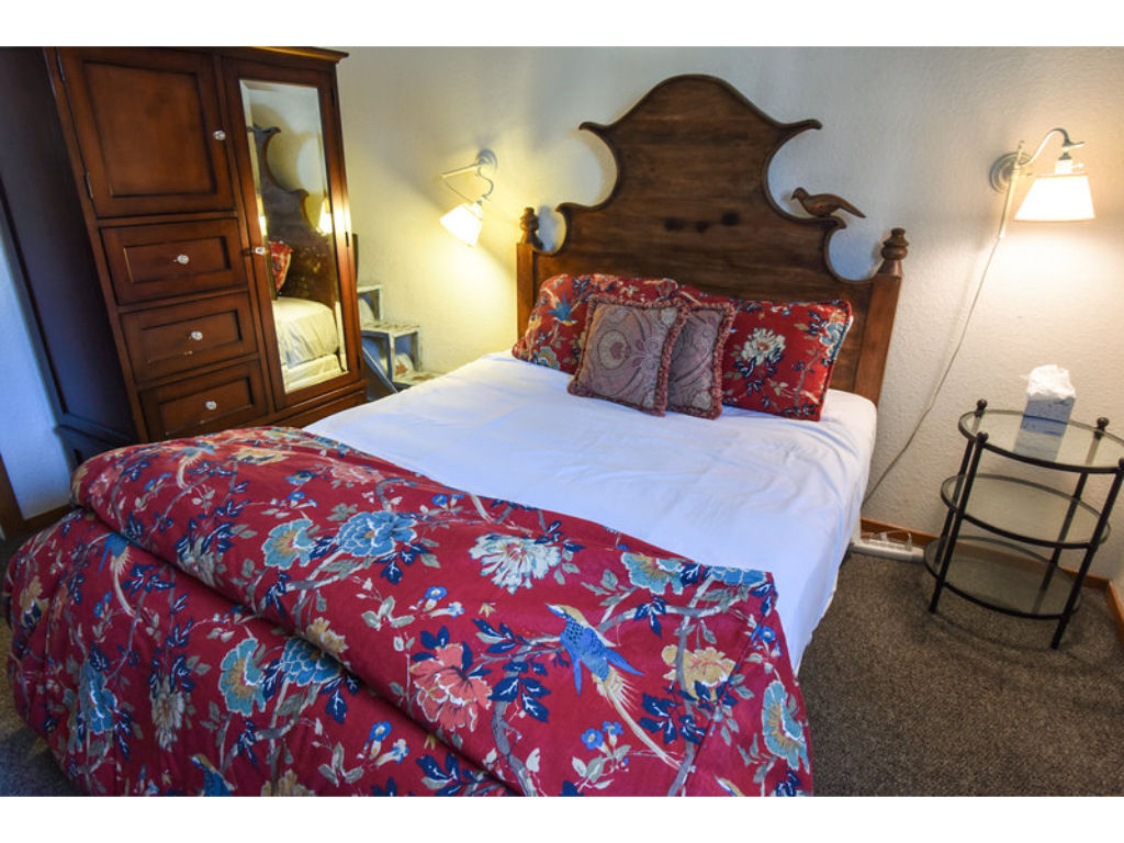 image This quaint bedroom boasts a beautiful decorative headboard and cozy bedding for a restful night's sleep.