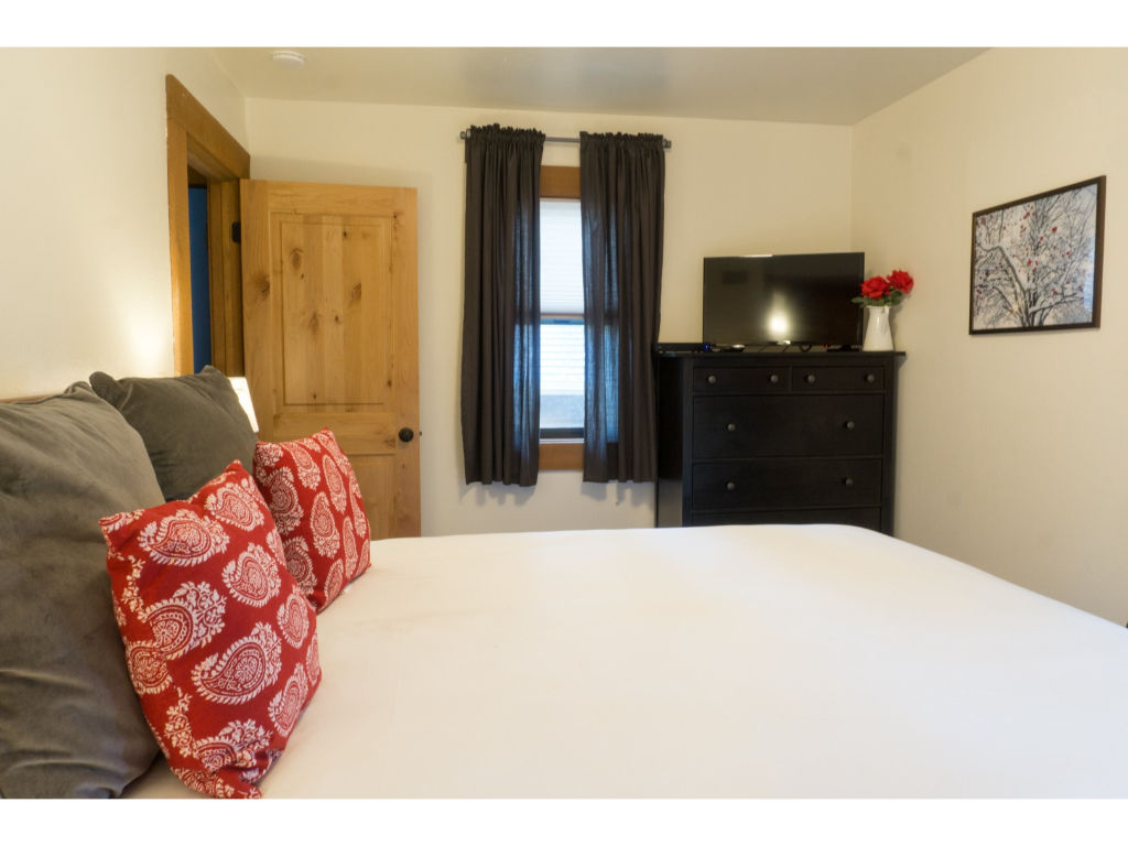 image Cozy bedroom with rustic charm, featuring wooden furniture, a comfortable bed, and vibrant pillows for a touch of color.