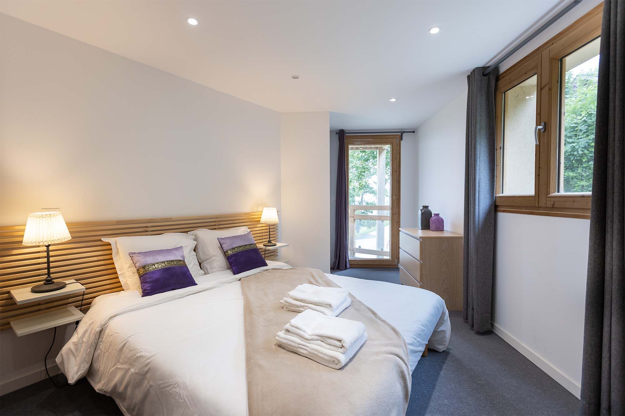 image Drift off to sleep in the cozy master bedroom featuring a plush double bed, soft lighting, and large windows that let in natural light and mountain views.