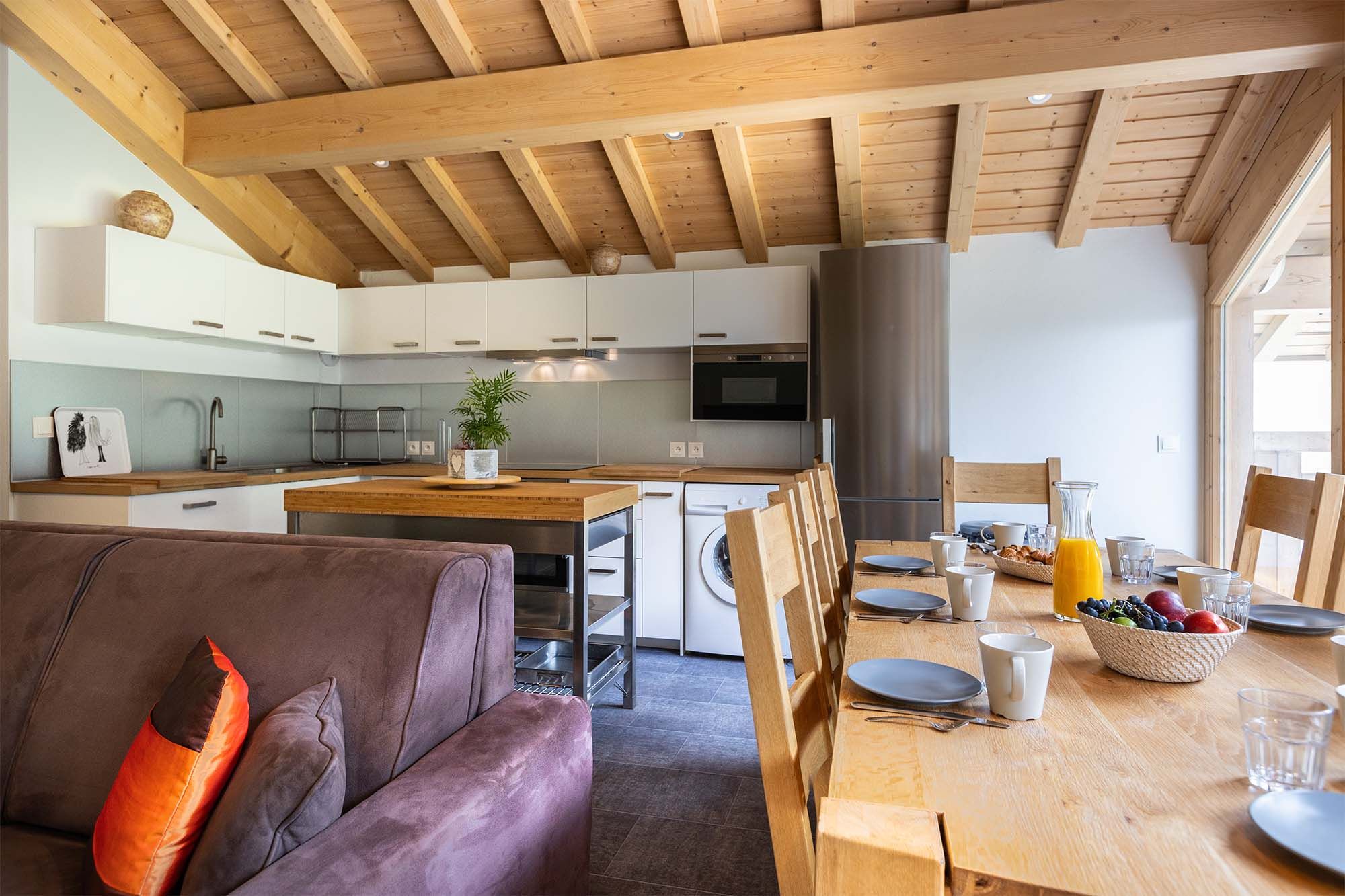 image Relax in this spacious living room with cozy seating and exposed wooden beams. The open-plan design seamlessly connects the living, dining, and kitchen areas, making it ideal for socializing and entertaining.