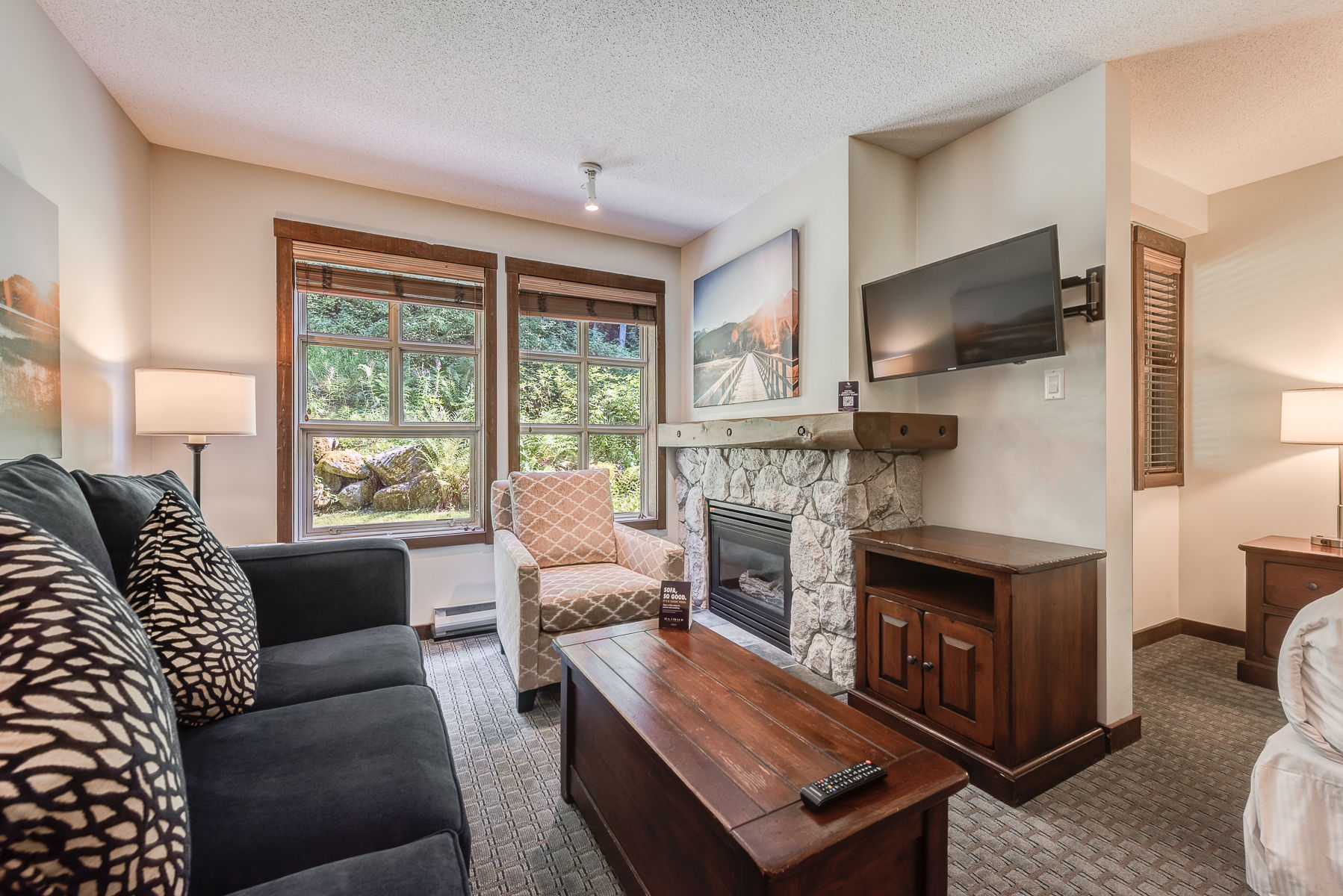 image Cozy living room with large windows, a TV, and comfortable seating overlooking greenery.