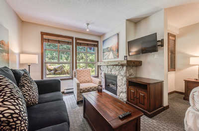 Cozy living room with large windows, a TV, and comfortable seating overlooking greenery.