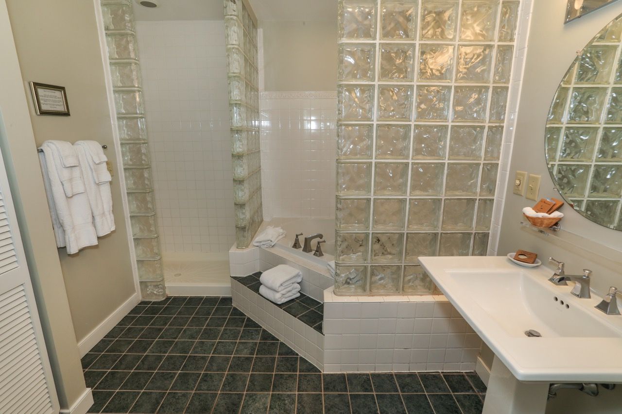 image Spacious bathroom featuring a luxurious soaking tub, sleek glass accents, and a modern pedestal sink.