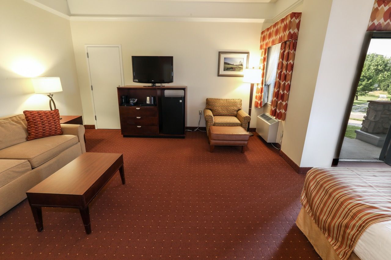 image Spacious suite featuring a plush bed, cozy seating area, and natural light from large windows.
