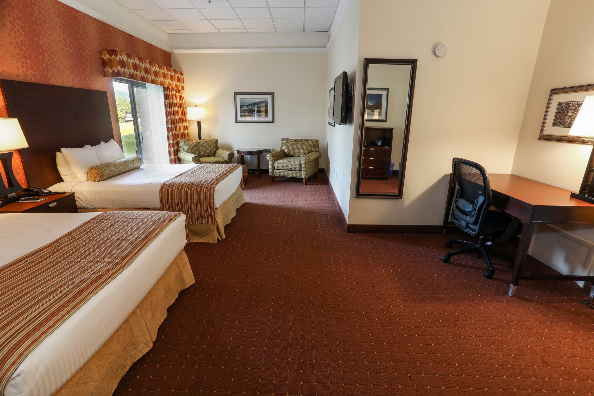 image Comfortable room featuring two cozy beds, a work desk, and natural light from large windows.