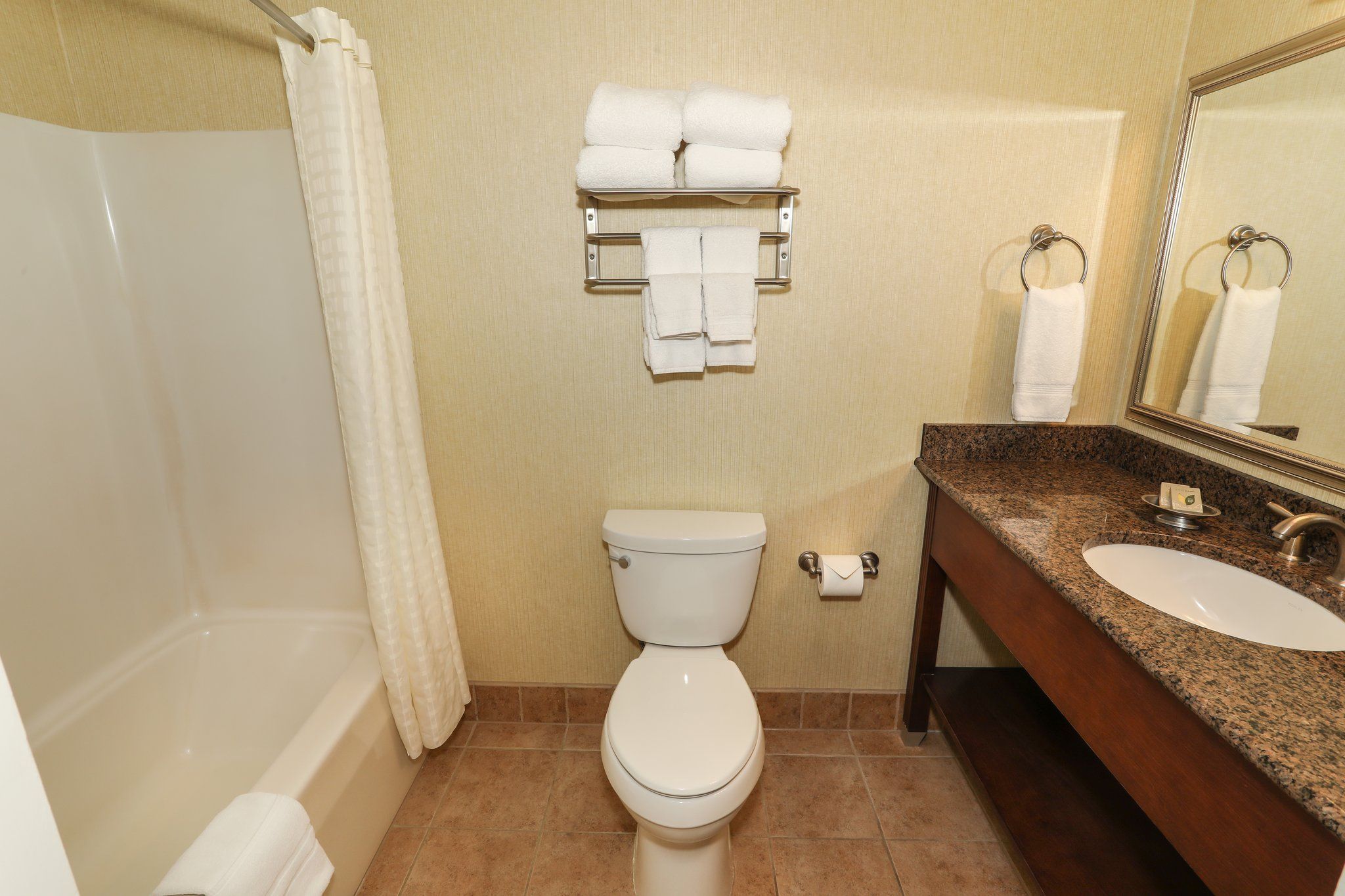 image Clean and modern bathroom with a shower/tub combo, granite vanity, and fresh towels.