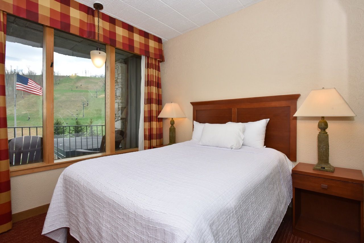 image Bright and inviting bedroom featuring a plush bed, soft lighting, and a window framing scenic outdoor views.