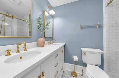 Elegant full bathroom featuring dual sinks, gold fixtures, and a sophisticated blue accent wall.