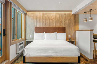 A serene bedroom with warm wooden accents, a plush bed, and large windows for an inviting and restful atmosphere.