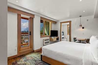 A bright and inviting room with a plush bed, large windows, and a door opening to scenic views, offering a seamless blend of comfort and nature.