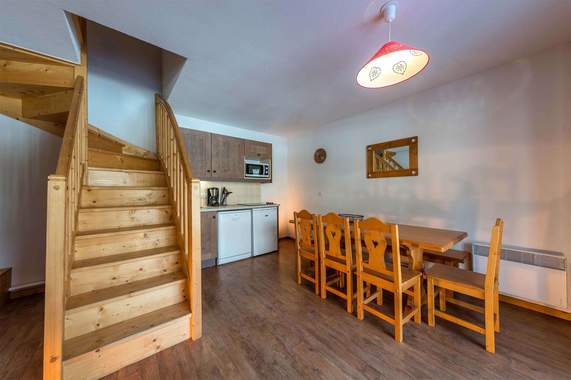 image Spacious duplex apartment featuring a cozy dining area and a wooden staircase leading to the upper floor.