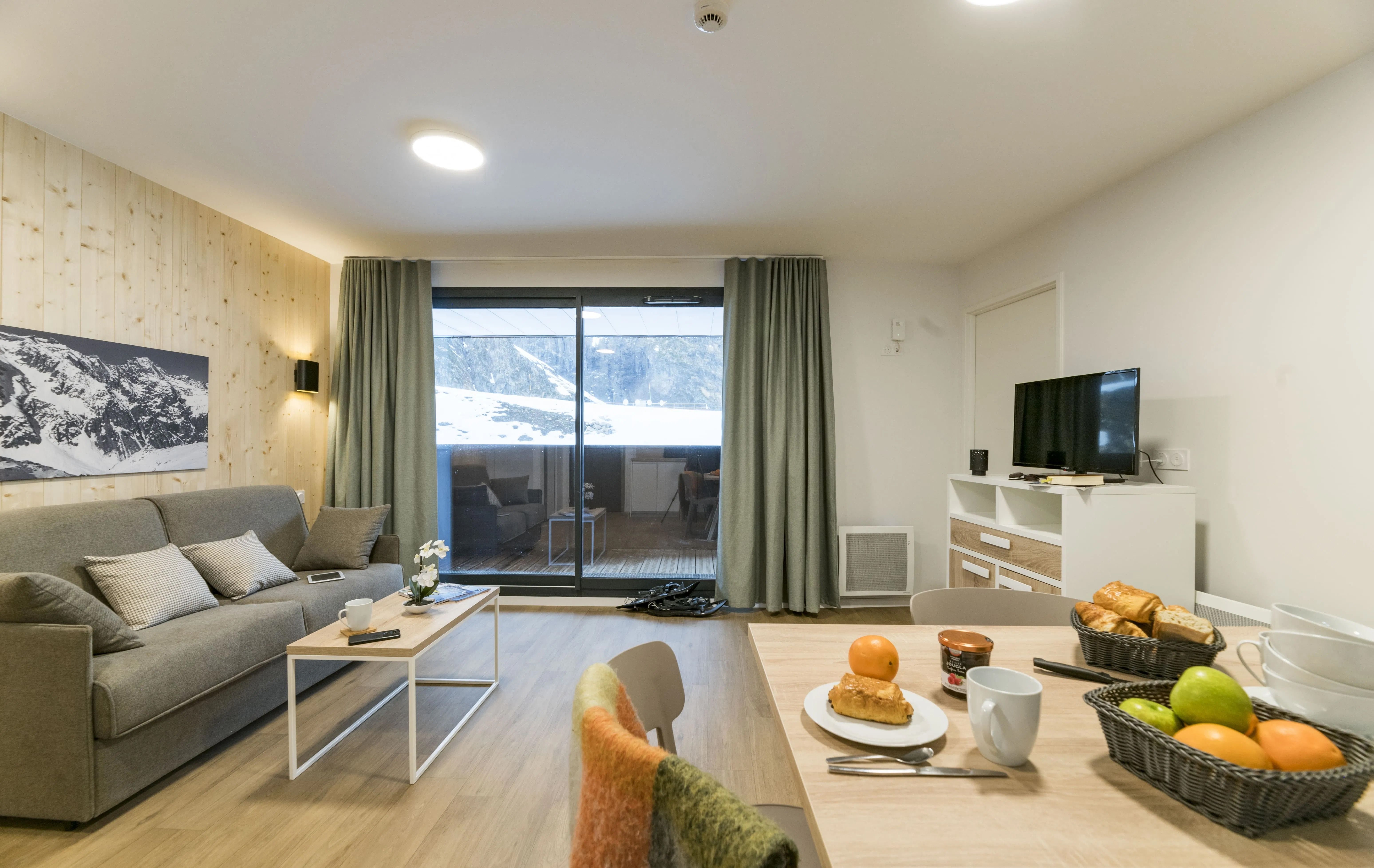 image Relax in the spacious living area, featuring a cozy sofa and a stunning view of the snow-capped peaks through the sliding glass doors.