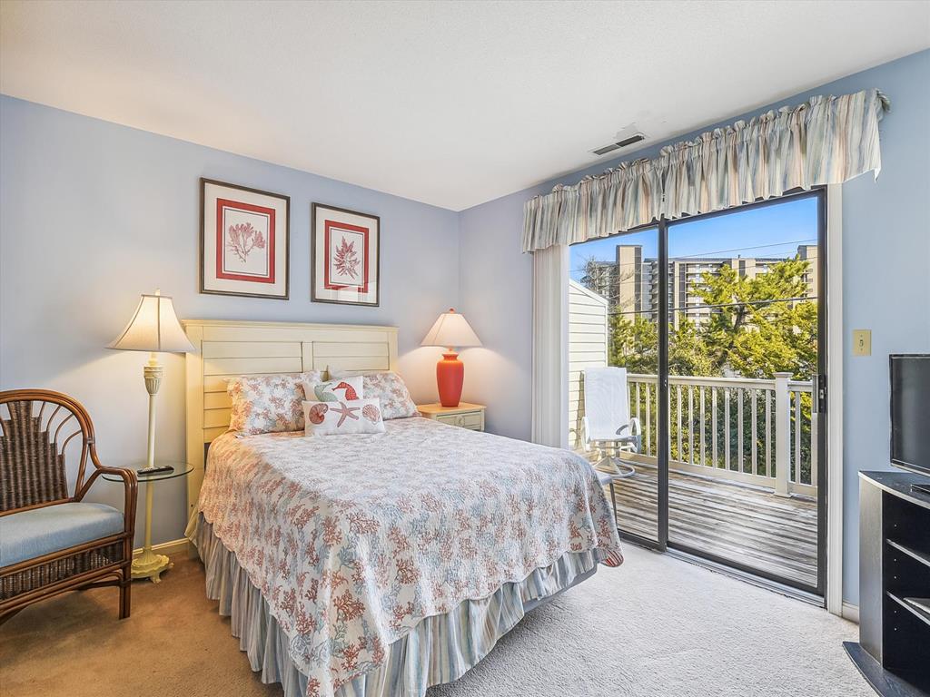image Unwind in the spacious master bedroom featuring a private balcony, decorated with beachy charm and plenty of natural light, making it a perfect retreat after a day by the shore.
