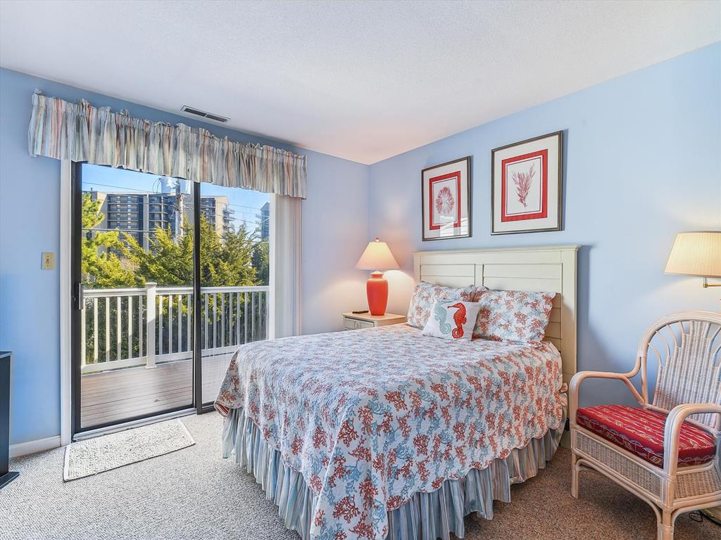 image Rest easy in the beautifully decorated master bedroom featuring a queen bed and sliding glass doors leading to the deck, offering a perfect setting to start and end your beach days.