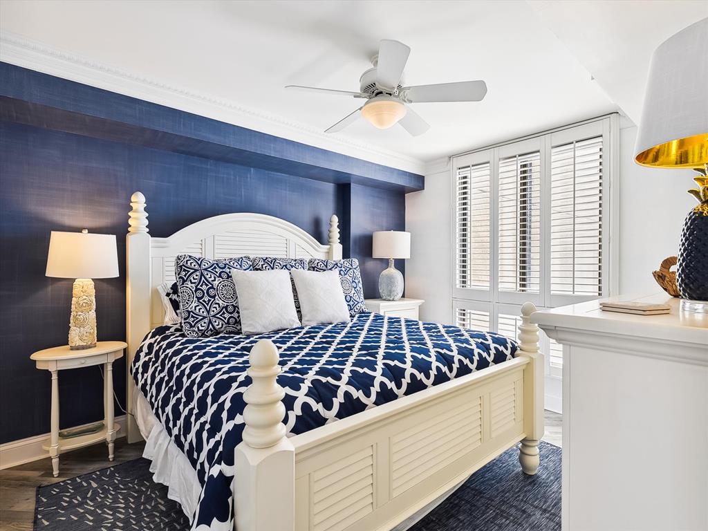 image The serene master bedroom boasts a rich navy color palette, stylish decor, and large windows, inviting both comfort and tranquility with a refreshing ocean breeze.