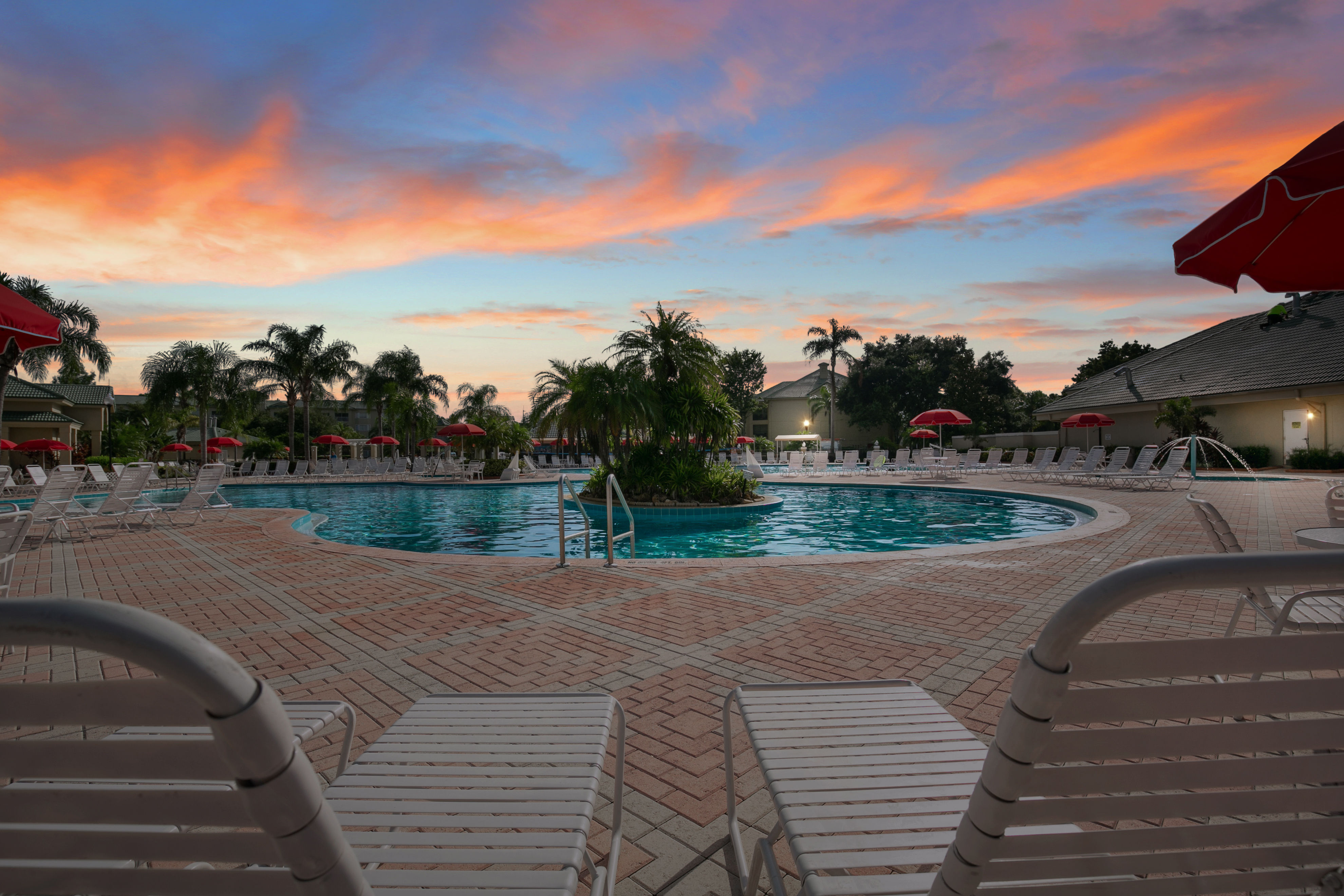 image Dive into relaxation at the stunning outdoor pool surrounded by palm trees and lounge chairs, set against a beautiful sunset backdrop.